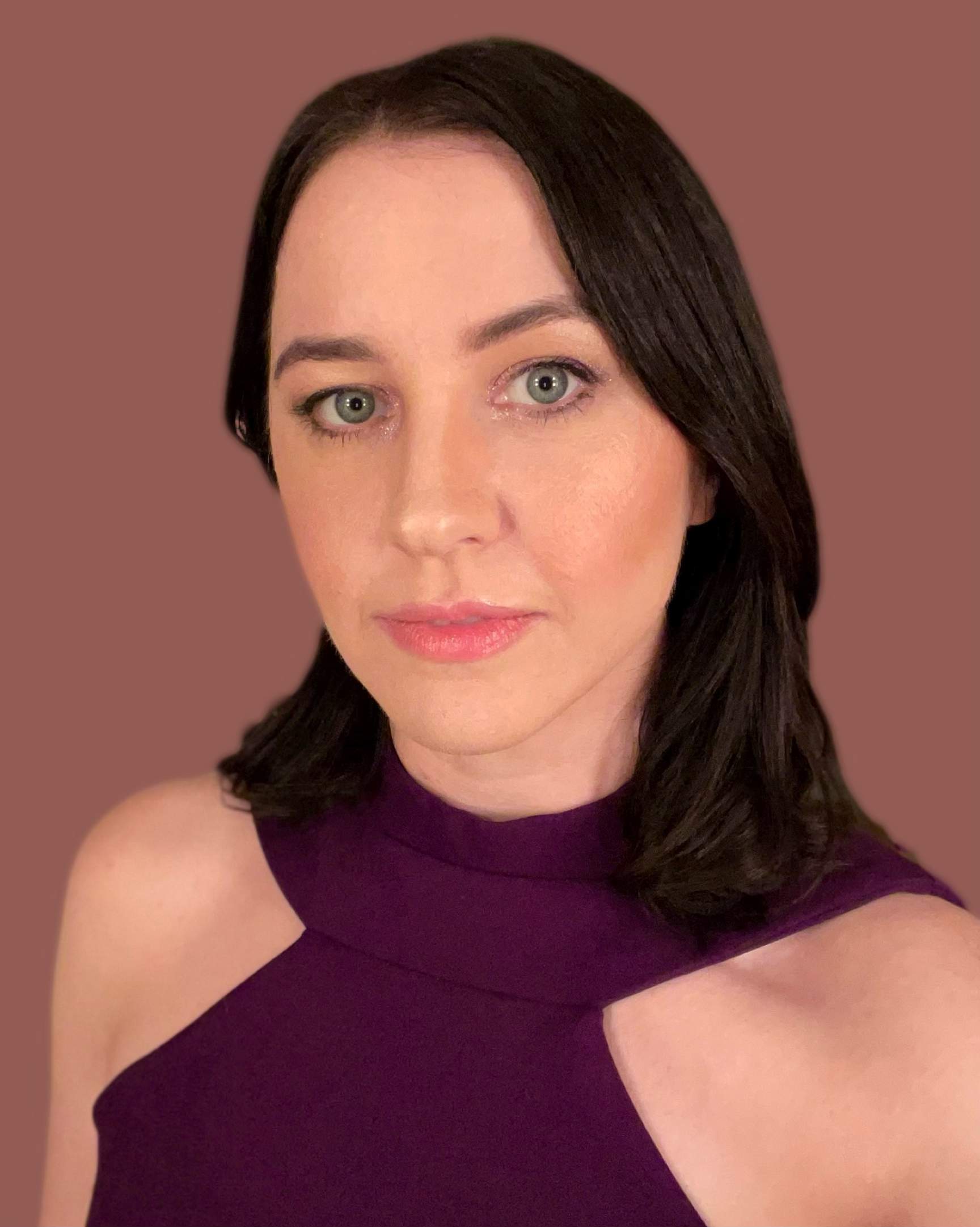 Sarah Colby's headshot. She has long, dark brown hair, bright red lips, pale white skin, and bright blue eyes that stare intensely into your soul.