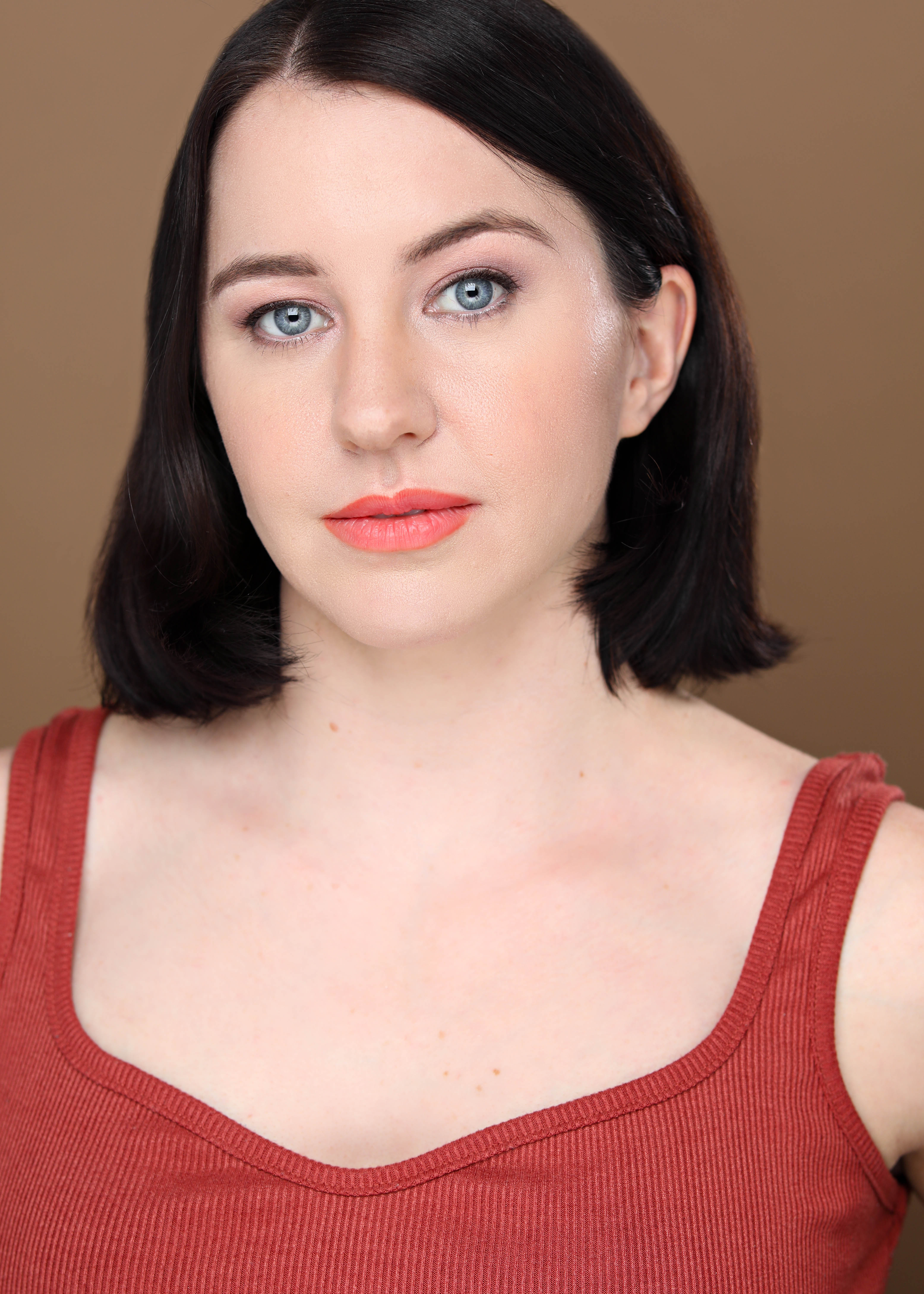 Sarah Colby's headshot. She has long, dark brown hair, bright red lips, pale white skin, and bright blue eyes that stare intensely into your soul.