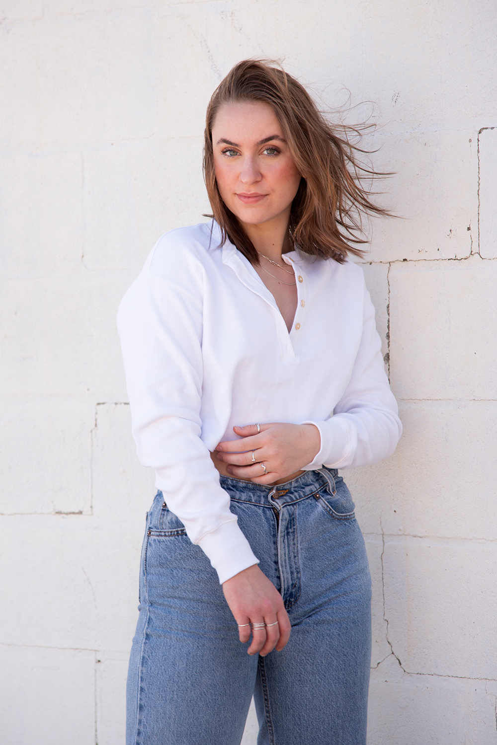 Female subject stands in front of white brick wall with blue jeans and white t-shirt for an urban style image