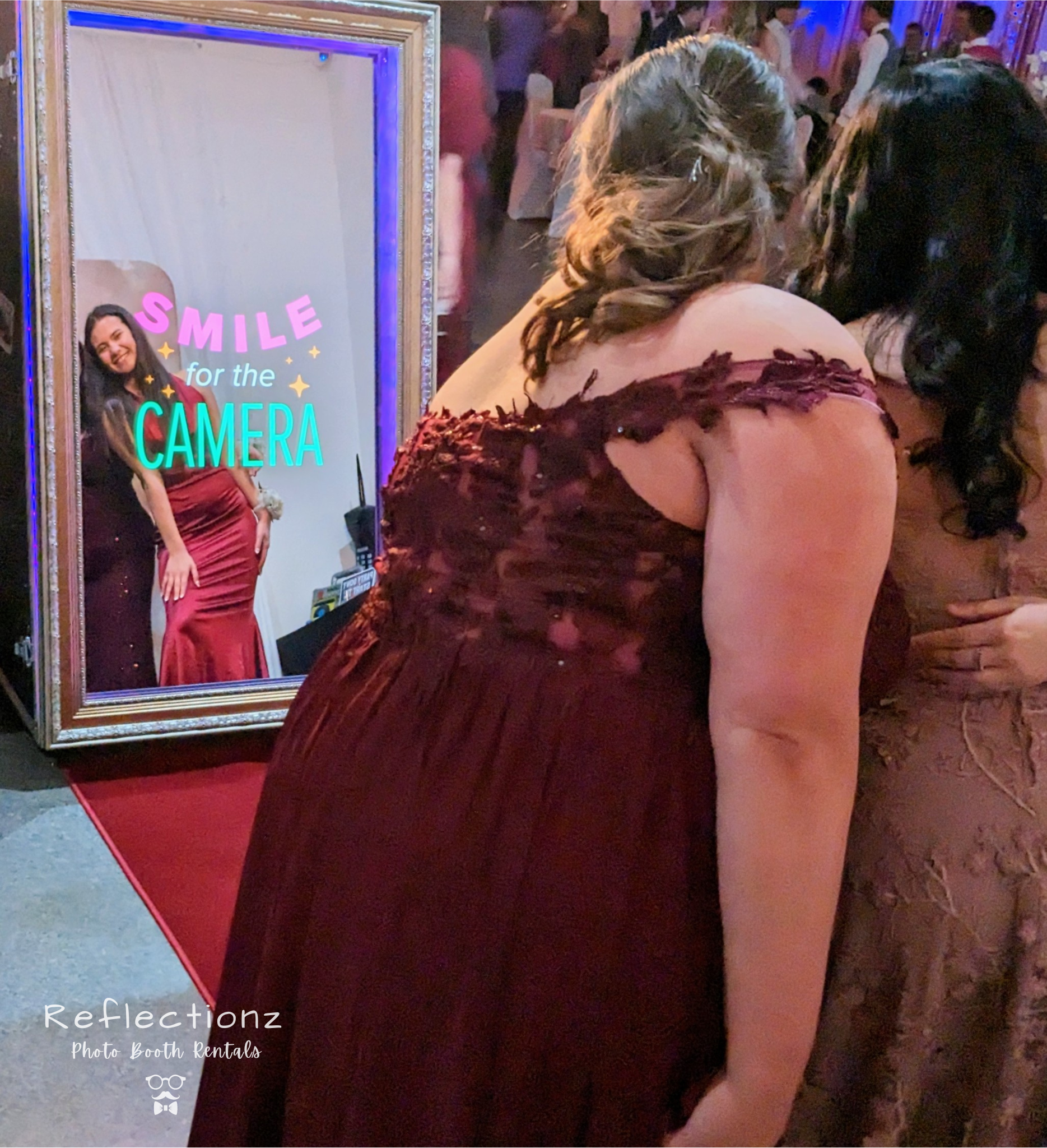 Guests posing in front of a magic mirror photo booth with 'Smile for the Camera' text.