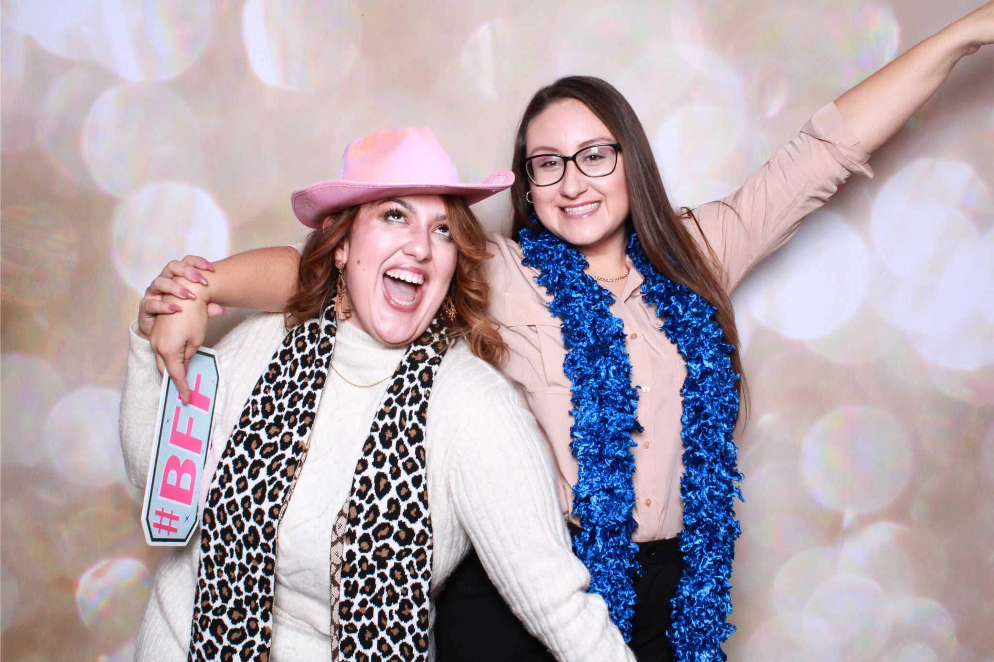 Two best friends having fun at a photo booth, wearing props and big smiles.