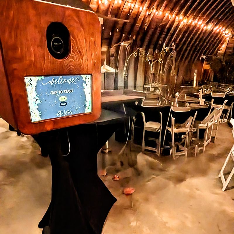 Photo booth setup in a rustic venue with wooden beams and string lights.
