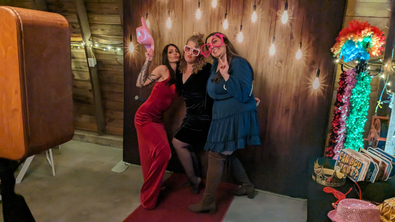 Three friends in dresses posing with fun props at a photo booth during an event.