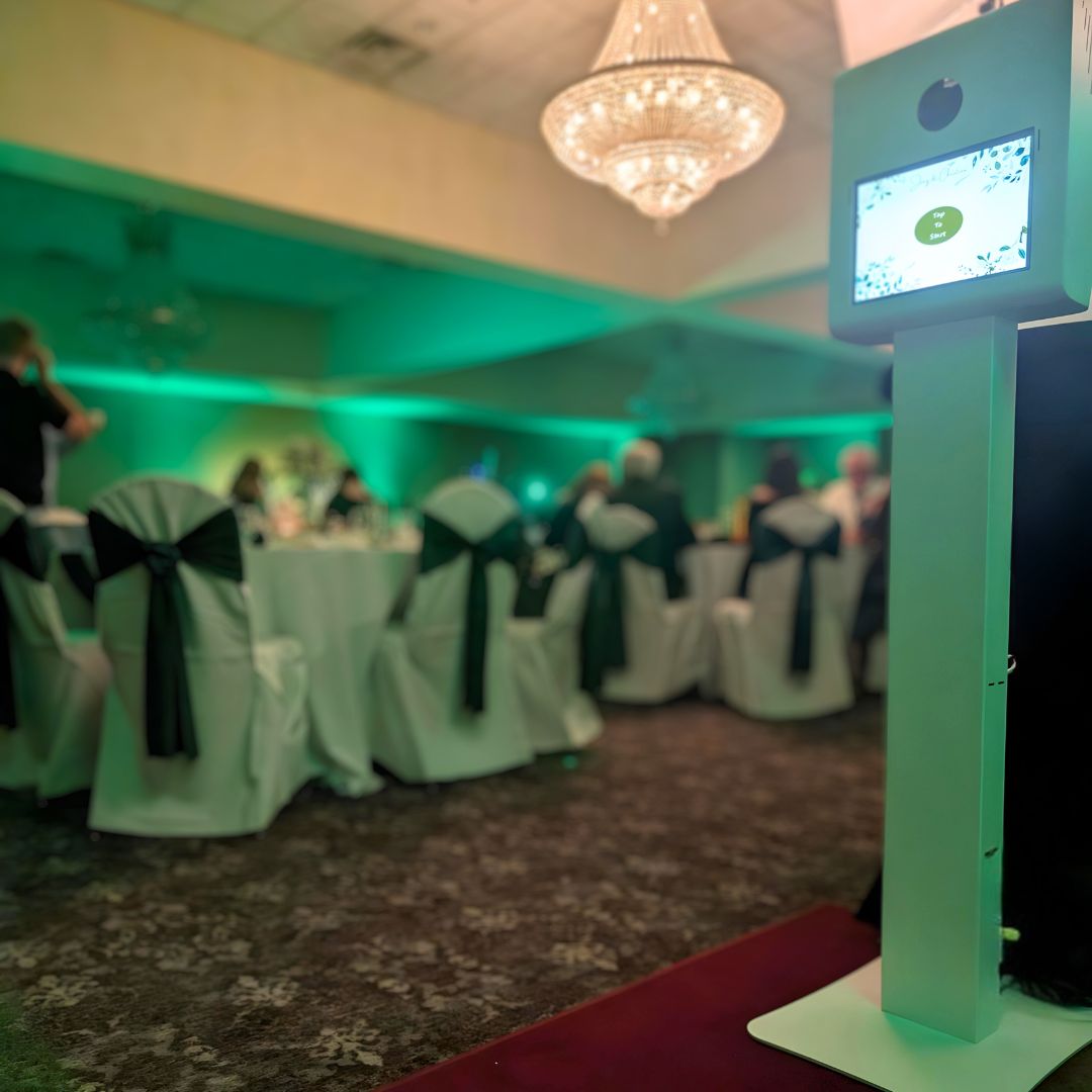 Photo booth setup at a green-lit event with elegantly decorated tables and chandelier.
